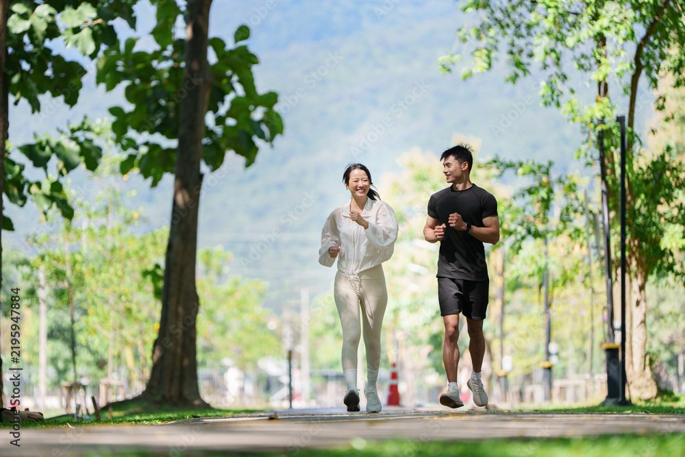 Fototapeta premium Smiling Asian couple jogging together in park for outdoor cardio workout