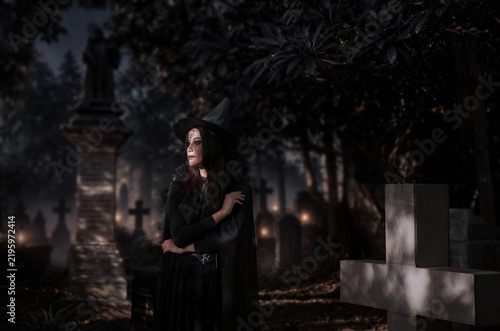 Quadro su tela A mysterious witch in a dark cemetery under a full moon, surrounded by glowing lanterns and howling wolves, creating a spooky Halloween atmosphere