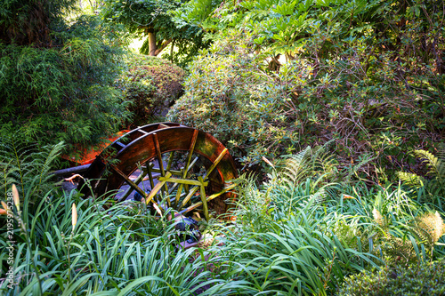 Rustic wooden water wheel surrounded by lush greenery in a garden