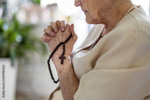 Elderly woman praying with rosary beads in her hands
