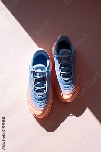 Two gradient sneakers are displayed on pink surface with natural light.