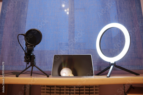 professional microphone and ring light setup in studio with blue backdrop and laptop for content creation and online streaming recording or streaming equipment.