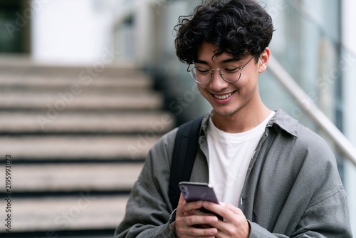 Young man happily using a smartphone against a blurred staircase background