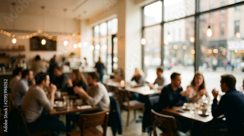 Blurred cafe interior filled with people sitting at wooden tables during a bright sunny afternoon