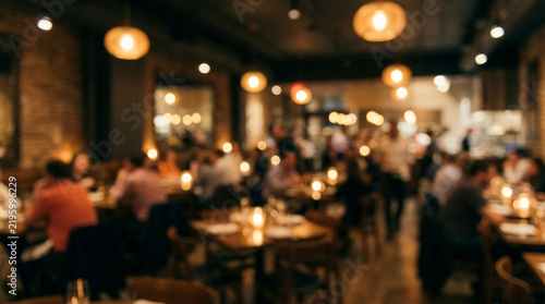 Blurred interior of crowded restaurant featuring warm golden lighting and numerous dining guests at night