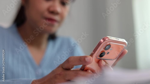 Close up view of Asian woman holding elegant mobile phone in hands tapping display screen to verify online client order details while sitting in calm work environment indoor
