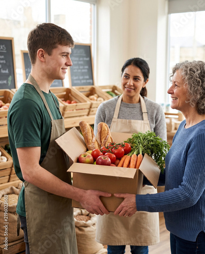 Smiling grocery store clerk handing box of fresh food to senior customer
