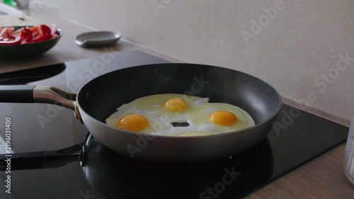 Three sunny-side up eggs frying in a non-stick skillet on an induction stovetop in a modern kitchen.