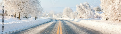 Snowy road winding through a winter landscape with frost covered trees and houses