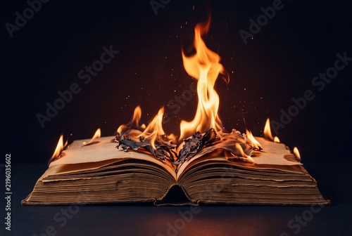 An old open book burning with bright flames against a dark background