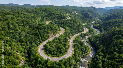 Aerial view of a winding asphalt road cutting through a dense green forest mountain