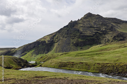Foto Skoga River curves through grassy banks below a rugged mountainside in Iceland