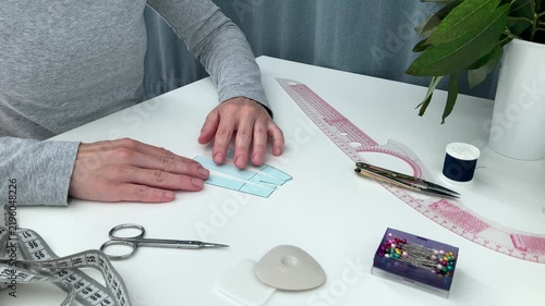 The woman lays out a small skirt pattern on a white table; the lady is learning to work with the clothing mockup and sewing supplies. The concept of acquiring a new hobby and practical skills