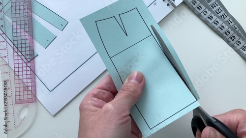 The woman cuts out a smaller pattern for the skirt with scissors, but this is the stage of developing the future garment item. The concept of clothing design, construction, and custom tailoring