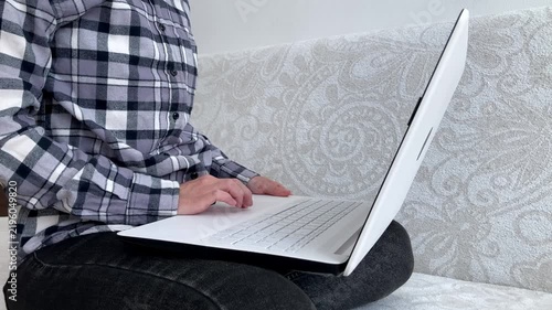 The woman is completing work tasks on a laptop in a comfortable home environment. The topic is the modern employment format, freelancing, independent work, and mobile office. Side view