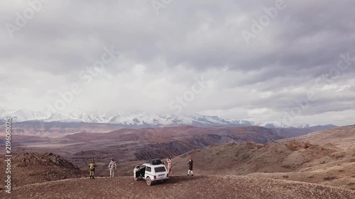 Drone view a group of men are standing next to a car with a stunning view of the endless steppe and snow capped mountain peaks. Passion for travel, overcoming obstacles, and extreme tourism.