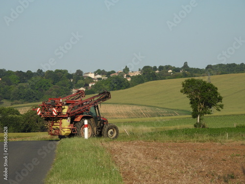 Fotografie A red tractor with a large sprayer stands beside a narrow road