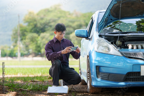Insurance agent taking photo of broken down blue car for claim report