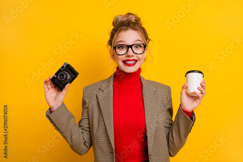 Konstfotografi Young stylish woman holding a camera and coffee cup in front of yellow backgroun