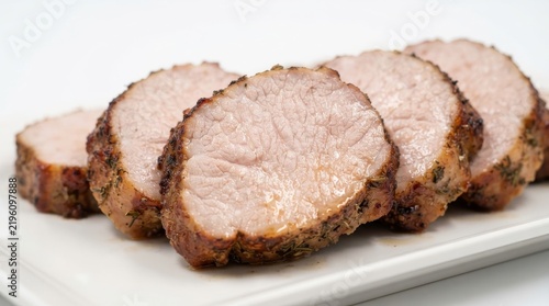 Several thick slices of roasted pork loin seasoned with herbs, arranged on a white rectangular serving plate against a plain white background