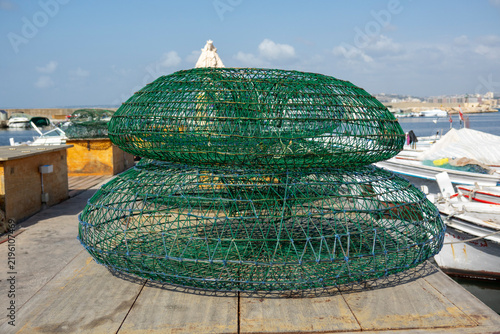 Green wire fish traps are stacked on a wooden pier overlooking the fishing harbor, South Governorate, Tyre, Lebanon
