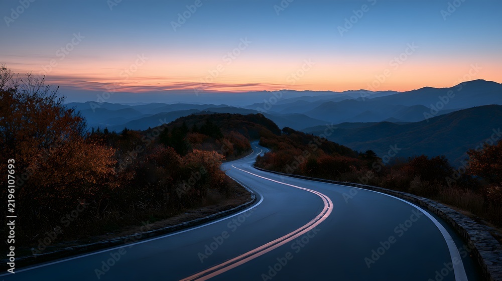Obraz premium Curving mountain highway at dusk with soft sunset colors and distant blue mountain silhouettes