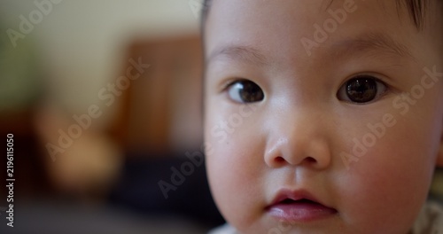 Obraz na płótnie An innocent Asian toddler looks directly at the camera with curiosity, a soulful close-up portrait representing childhood development, hope, and the future from home