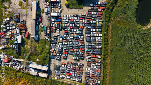 Aerial view of a car scrapyard with rows of wrecked vehicles, scrap metal, and industrial debris in Milan, Lombardy, Italy.