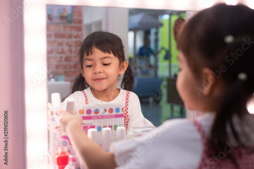 Obraz na plátně Happy young girl playing with toy makeup in front of a mirror, exploring beauty