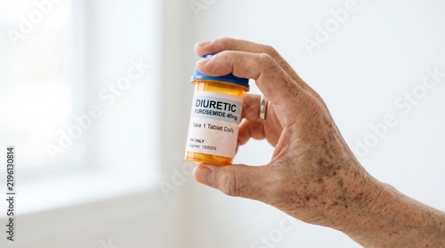 Close up of an elderly hand holding a prescription bottle of diuretic furosemide. Senior medical care and hypertension treatment