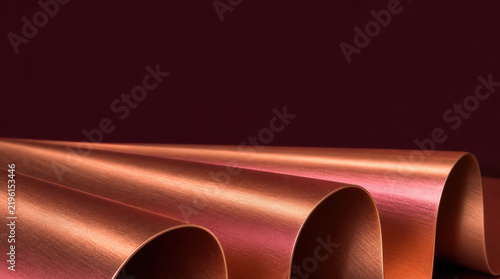 Copper sheet shaped into four broad accordion folds with warm metallic texture and dramatic lighting, creating abstract industrial background with sweeping diagonal lines and rich color contrast