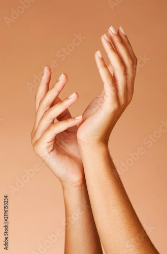 Close-up of elegant woman's hands with neat manicure gestures against a beige background.