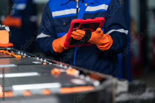 Close view of technician using digital tablet beside EV battery pack during automotive diagnostics, combining computerized inspection with high voltage component checks in modern automotive workshop.