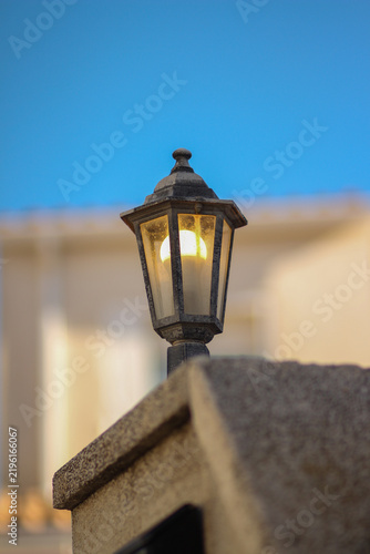 Glowing Vintage Street Lantern Against Blue Sky and Historic Stone Architecture