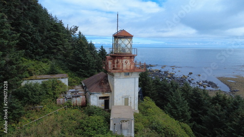 Behind a lighthouse on a cliff, looking out to sea.