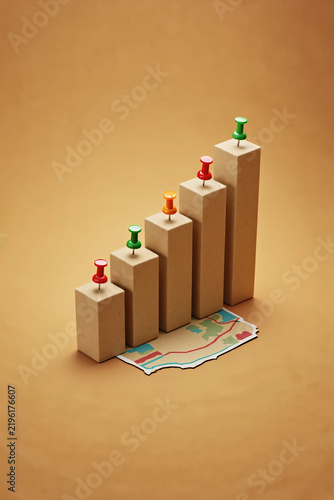 Wooden blocks forming a rising bar chart graph decorated with colorful push pins resting on a textured brown paper background representing business growth financial analytics and corporate success