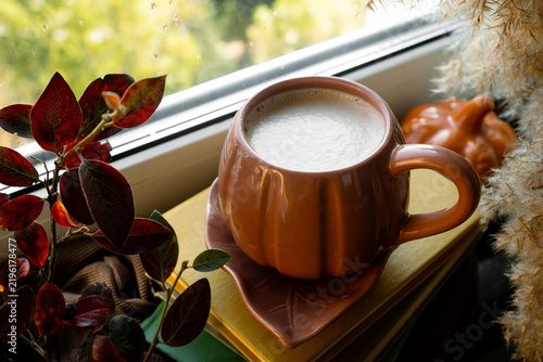 Mug of cappuccino coffee, books and autumn decoration on windowsill. Warm cozy fall vibes.