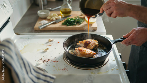Chef pouring dark sauce onto sizzling chicken in a busy kitchen