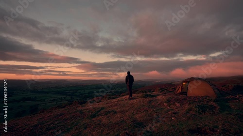 A man standing outside his camping tent on a hill in amazing sunrise weather