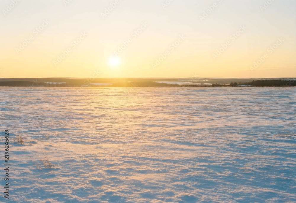 Fototapeta premium Winter landscape at sunrise, serenity and peace with golden light over a vast snow covered field in a cold rural environment during early morning