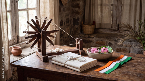 Traditional Indian Charkha Spinning Wheel with Khadi Cloth, Vintage Spectacles, and Tricolor Ribbon in a Rustic Interior Setting