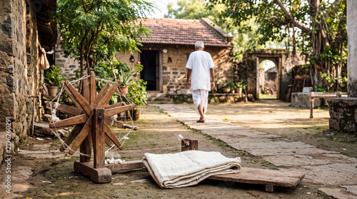 Traditional Wooden Charkha Spinning Wheel and Hand-Spun Khadi Cloth in a Peaceful Indian Village Courtyard with an Elderly Man