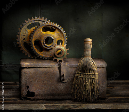 Still life of old rusted gears on old rusted box, with old whisk broom, on wooden table