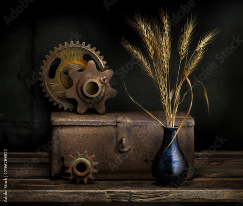 Still life with old rusty gears, rusty box, and wheat stalks in antique vase.