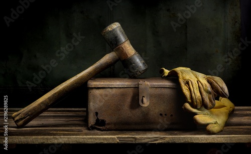 Old hammer and work gloves resting on rusted metal box in vintage still life.
