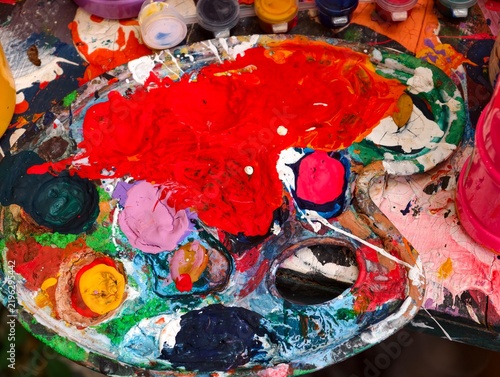 Artist's palette with colorful acrylic paint mixed together, red paint texture foreground.