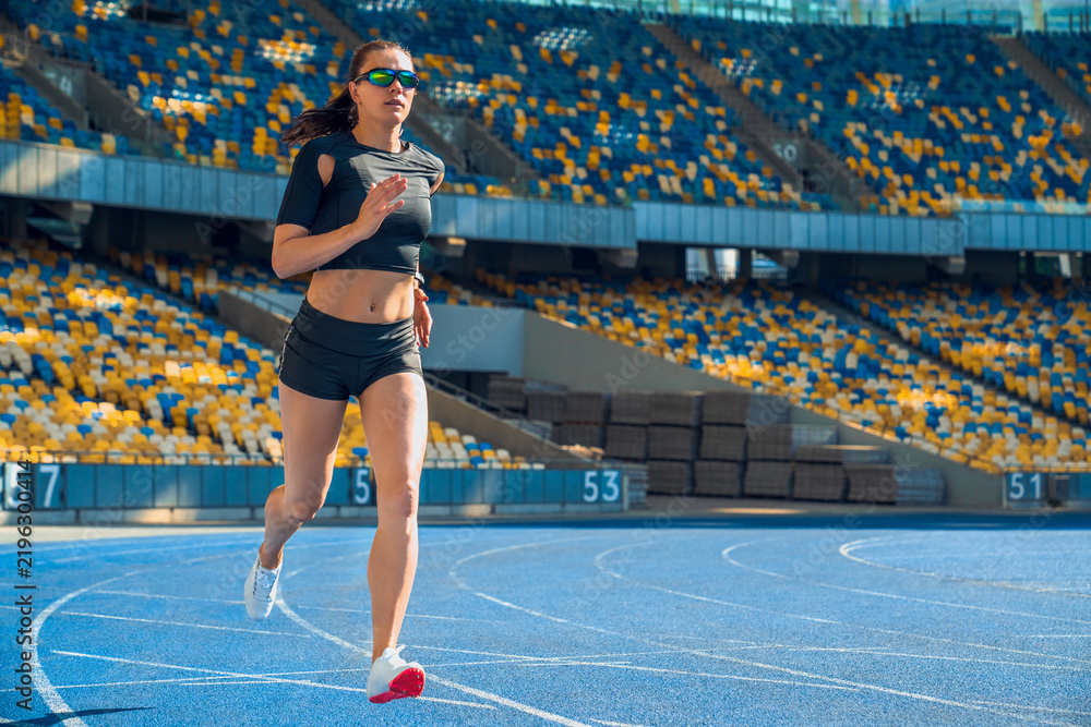 Fototapeta premium Female athlete sprinting on running track in stadium, woman runner practicing sprint training, sports competition, speed workout, endurance, fitness exercise and athletic performance concept