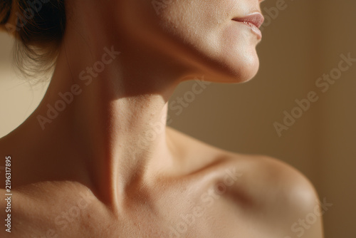 Soft shoulder and graceful neck in warm light with gentle shadow falling across beige skin, elegant minimal portrait conveying calm and subtle mood