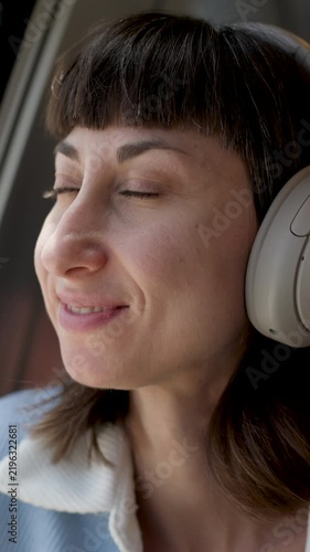 vertical shot. Young woman listening to music in earphones while traveling by train. relaxed face. passenger of the train. 
