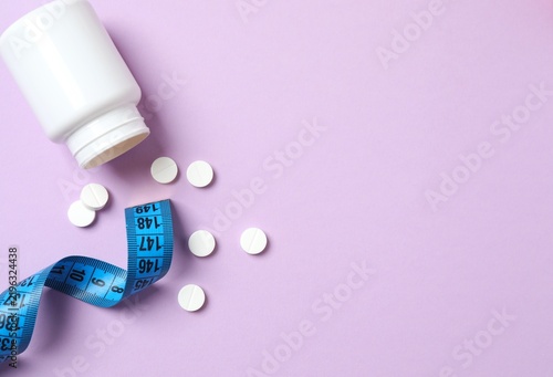 White jar of weight loss pills and measuring tape on color background